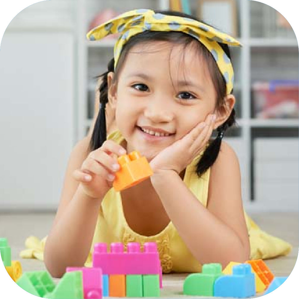 Bright smiling Asian girl playing with colourful building blocks, promoting early childhood education and speech development through engaging activities.