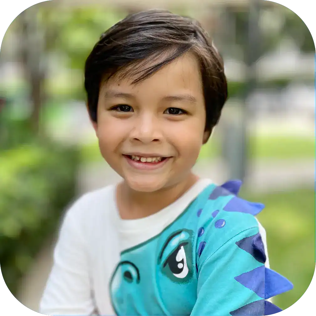 Happy young boy smiling outdoors, wearing a colourful cartoon dinosaur shirt, promoting children's speech therapy and early language development services in Australia.