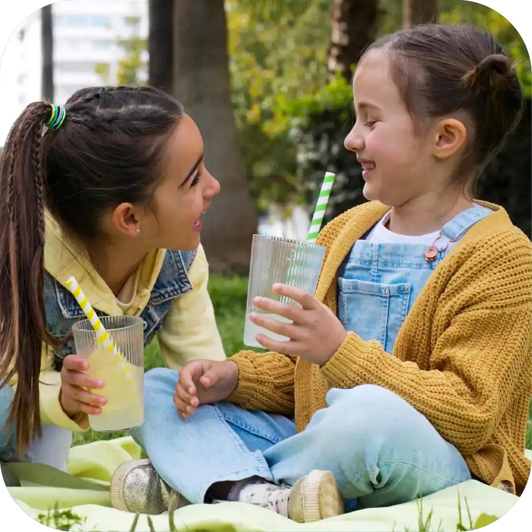 Smiling young girl and woman enjoying a picnic outdoors, sharing drinks and conversation, promoting communication skills and social interaction as part of Chatterbox Speech programs.
