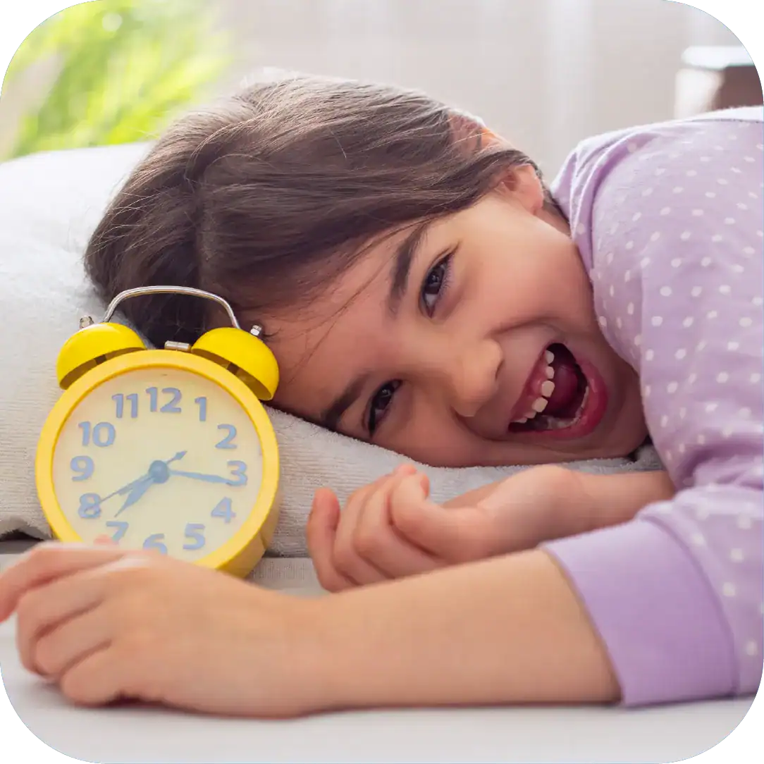Bright young girl laughing with yellow alarm clock on her bed, emphasizing speech therapy and early childhood development.